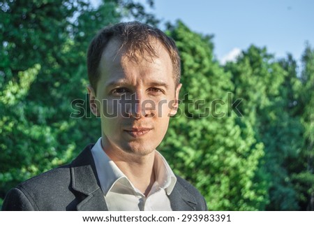 Young man in formal outfit looking seriously in camera, outdoors on the green background. Business man in a green zone or park. An image for topics of finance and business.