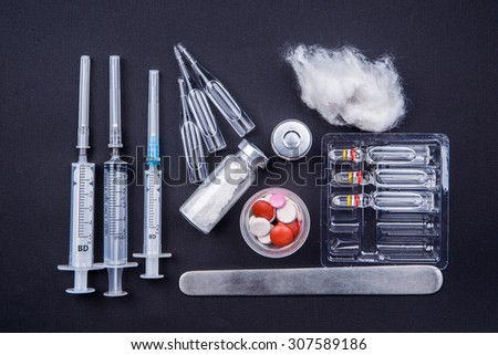 Medical objects still life seen from above on dark background. Syringes with pills and ampuls