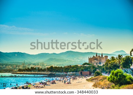 View of the beach of Palma de Mallorca with people lying on sand and the gorgeous cathedral building visible in background. Palma-de-Mallorca, Balearic islands, Spain.