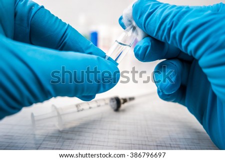 Doctor\'s hands in blue robber gloves preparing for a treatment procedure.  Glass vials and medications pills in background