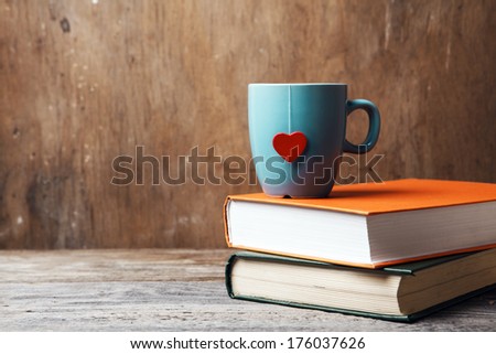 blue cup with red heart on green and orange books on grunge wooden table