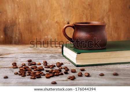 brown coffee cup on old green book and coffee beans on wooden table over grunge background