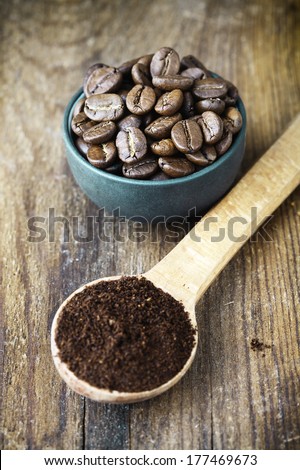 coffee beans in small blue cup and ground coffee in wooden spoon on aged wooden table