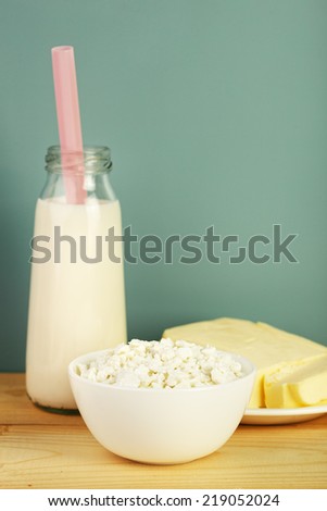 dairy products: school milk bottle with a straw, butter and cottage cheese on wooden table, vintage look