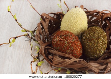 Easter decorations / cards hand-decorated easter eggs covered in spices and couscous with boxwood in a nest made of rattan on a wooden background / on the table with willow sticks