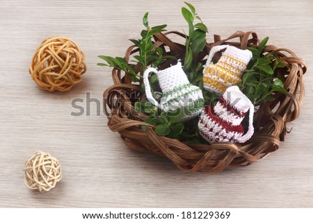 Easter decorations / cards handmade easter crocheted mugs with boxwood in a nest made of rattan on a wooden background / on the table with two rattan spheres / balls