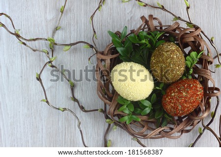 Easter decorations / cards hand-decorated Easter eggs an unusually covered in spices and couscous with boxwood in a nest made of rattan on a wooden background / on the table with willow sticks