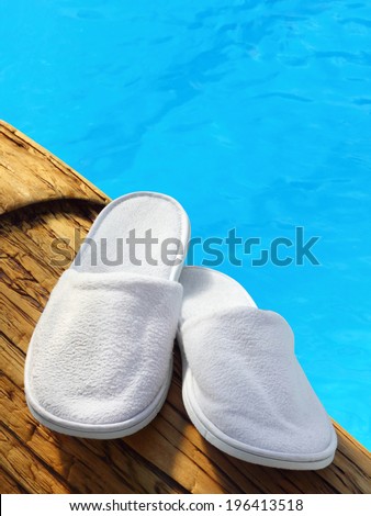 White hotel / home/ spa / wellness slippers on wood with swimming pool background with space for text - summer time
