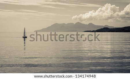 Distant sailboat on calm waters with mountains in the distance.  Black and white toned