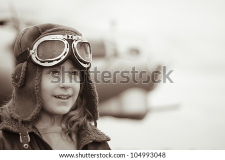 A confident young female pilot is gazing into the distance, wearing flight jacket / hat / goggles.  Bomber is visible in the background out of focus.