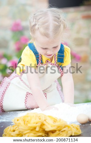 Girl preparing pasta dough on wooden table.