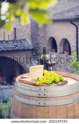 Red wine, pecorino cheese, grapes, bottle and glass on wooden barrel in the background of the Tuscan landscape, Italy