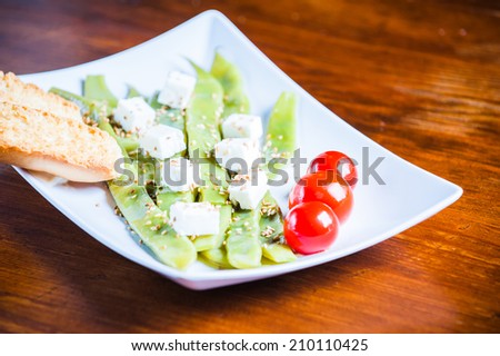 A plate of string beans with feta cheese and sesame seeds, decorated with cherry tomatoes and balsamic dressing