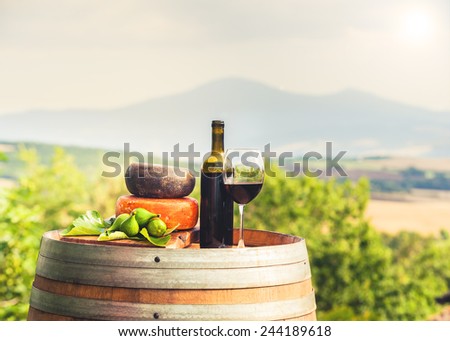Red wine, cheese, figs on a wooden barrel in the background of the Tuscan landscape, Italy