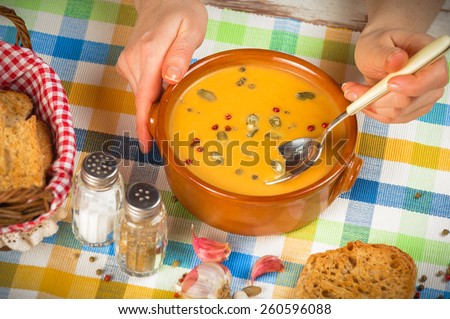 Homemade pumpkin soup and hands with a spoon on rustic table