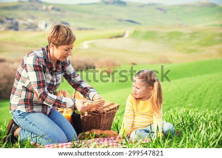 Mother and daughter arranged picnic on the green spring grass in the landscape of Tuscany.