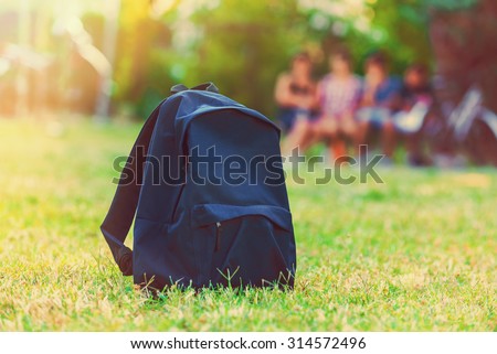 Blue school backpack standing on green grass with students in background