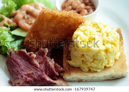 Cooked breakfast of crisply fried beef, scrambled eggs, toast bread, beans, triangle fried potato with salad