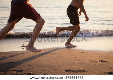 Two guys running on the beach at sunset playing football