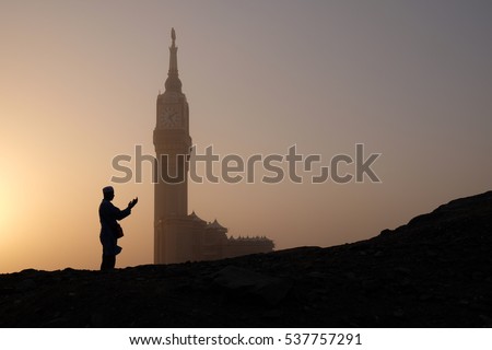 Silhouette of muslim man praying (doa) with Makkah Royal Clock Tower in the background.
