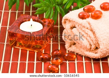 Spa scene with glass pebbles on towel, candle and green plant on bamboo