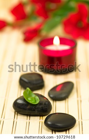Therapy stones, candle and flower on bamboo, focus on green leaf with waterdrop