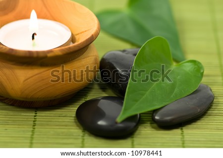 Spa stones with green leaves and candle on green bamboo