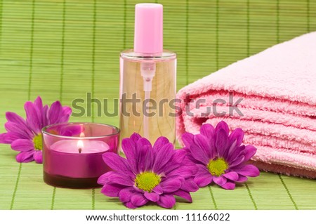 Wellness scene with fragrance bottle, towel, candle and flowers on green bamboo