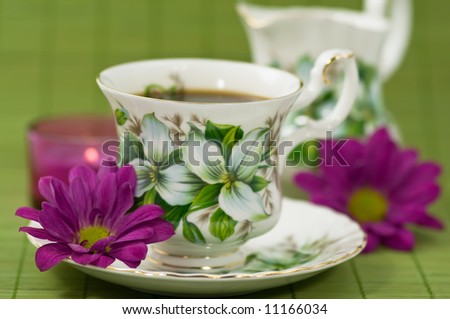 Cup of coffee and creamer with candle and flowers on green bamboo