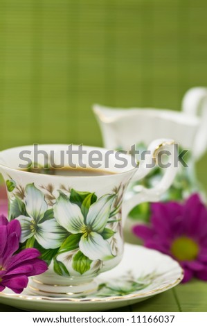 Cup of coffee and creamer with flowers on green bamboo