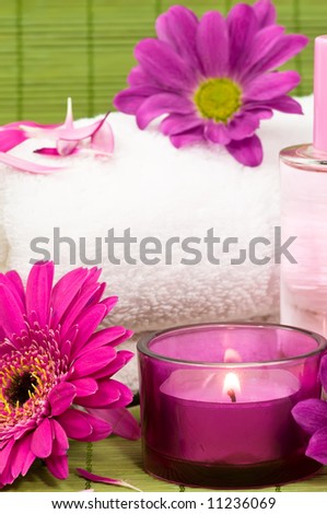 Towel with flowers and petals, candle and fragrance bottle on green bamboo
