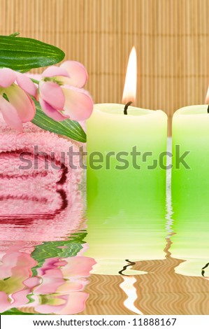 Spa candles, towel and decoration flowers with water reflection