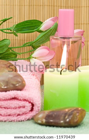 Fragrance bottle with candles, stones, towel and decoration flower on bamboo background, focus on bottle