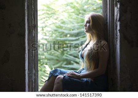 Girl standing at the window/ A girl with long blond hair standing in a dark room with an open window. Trees outside the window.