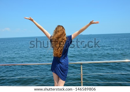 Girl with hands lifted up/  Long-haired girl standing with hands raised up on the beach.