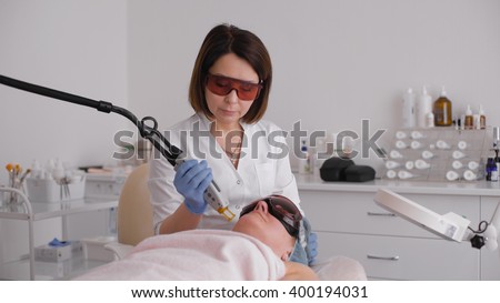 Cosmetician in safety glasses using laser for facial treatment in cosmetology clinic. light medical office