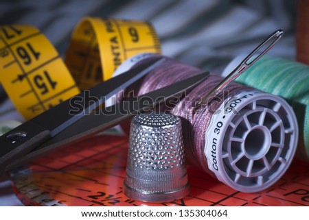 Sewing Thread Spools, Metal Scissors, Metal Thimble, Sewing Ruler and Needle on Fabric.