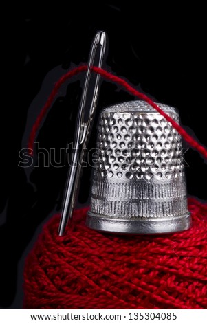 Sewing Thread Through the Eye of a Sewing Needle and Metal Thimble on Sewing Thread Spool Isolated on Black