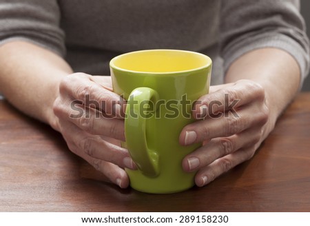 close-up on mature woman\'s hands thinking and relaxing at breaks with a green cup of coffee or tea