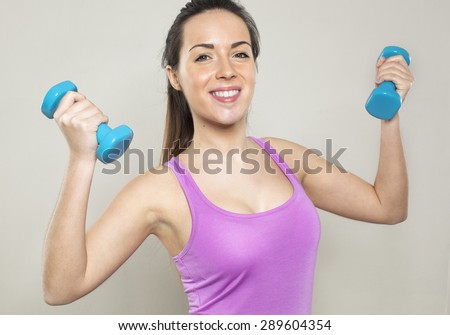 joyful athletic woman wearing sportswear holding two dumbbells for workout and toned arm muscles
