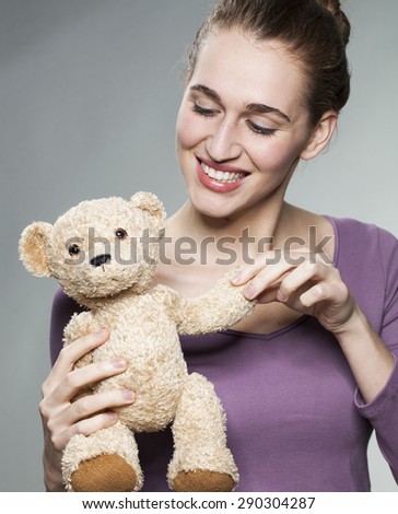 smiling young blonde woman playing with her teddy bear with tenderness for child memories