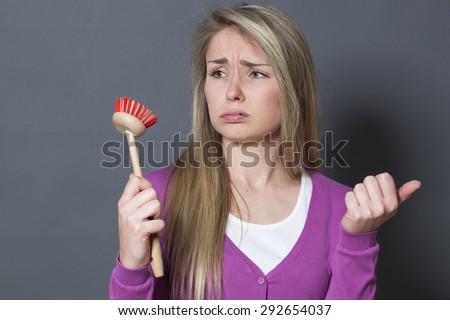 annoyed young blond woman displaying dish brush for pain about washing dishes role