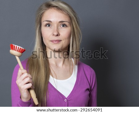 smiling young blond woman wearing purple sweater holding dish brush with serenity and calm
