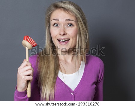 laughing young blond woman wearing purple sweater holding dish brush with fun and surprise