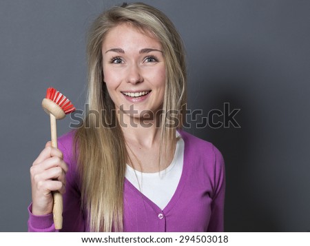 laughing young blond woman wearing purple sweater holding dish brush with fun and excitement