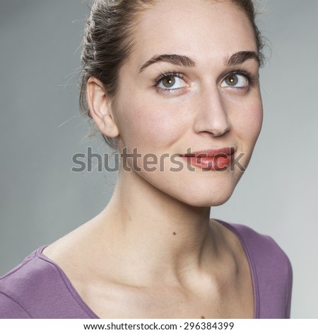 closeup on gorgeous young woman smiling with eyes looking up, thinking about her future with optimism, wearing purple sweater in studio shot