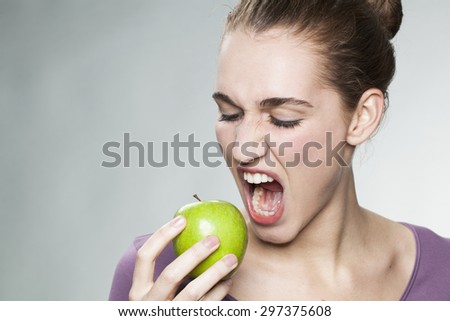 hungry young woman ready to bite green apple with anger for frustrating diet