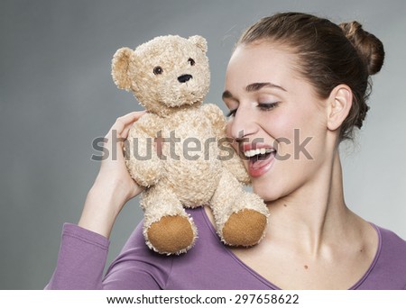 playful young blonde woman holding her teddy bear on her shoulder with tenderness for beautiful memories together