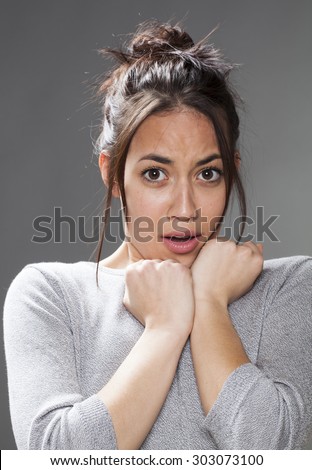 fear concept - scared mixed race 20s woman with brown hair protecting herself with both hands on shoulders,studio shot