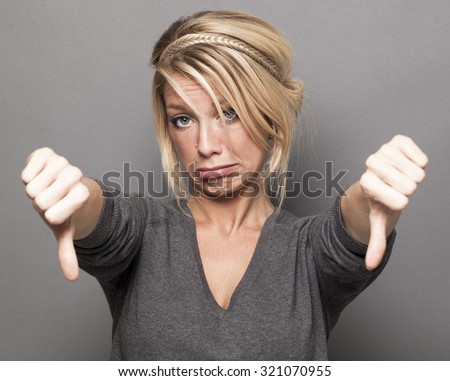 disappointment concept - sad young blond woman making double thumbs down for disagreement or discouragement